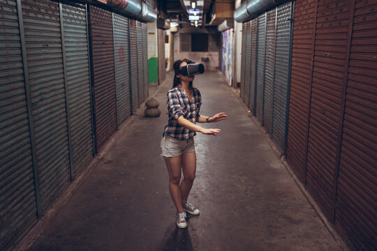 Calm female standing on narrow shabby street and experiencing virtual reality while wearing wireless VR goggles