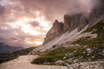 Majestic summer sunset over a deserted high mountain trail running at the foot of towering rocky peaks. Dolomites, Northern Italy.