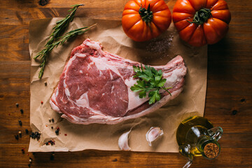 Top view of raw beef placed on craft paper on table with fresh tomatoes and olive oil arranged with condiments and garlic