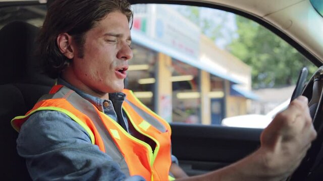 Construction worker sitting in truck feeling ill, using mobile phone to check in with tele-medicine doctor on video call.