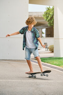 Vertical photo of a boy with a printed shirt and shorts skating a skateboard in a park