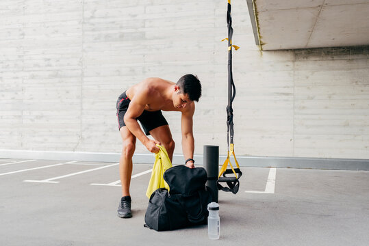 Focused male athlete with naked torso standing near sports bag and preparing for training on street