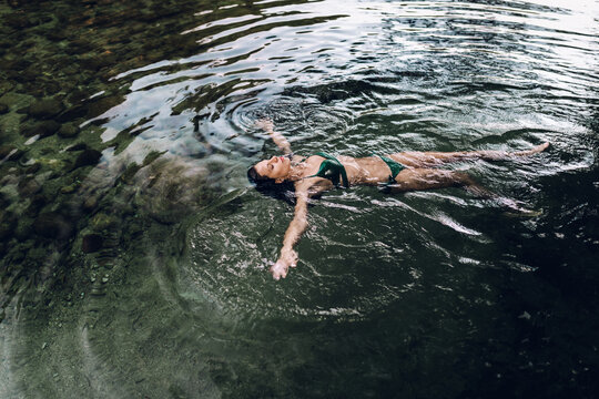 Relaxed female in bikini lying on water of pond and enjoying summer vacation with closed eyes - Powered by Adobe