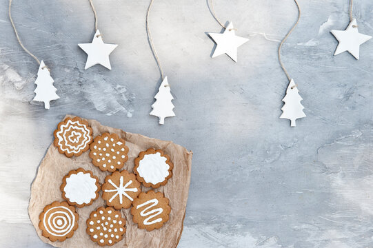 Plate with assorted gingerbread cookies with white icing placed near gray wall decorated with craft star and tree shaped paper items