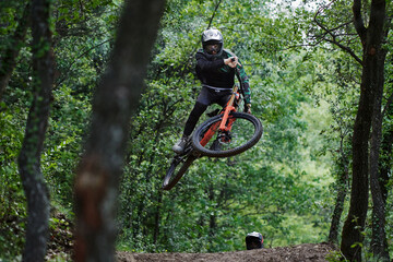 Male cyclists in protective helmets and costumes performing dangerous stunts on bikes for downhill on trail in forest