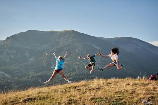 Company of delighted friends jumping on hill in mountains while enjoying freedom during summer vacation