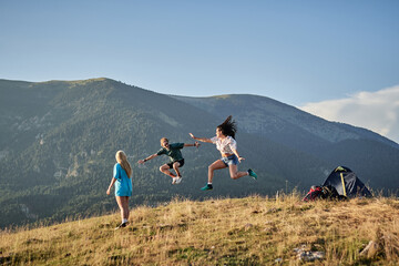 Company of delighted friends jumping on hill in mountains while enjoying freedom during summer vacation