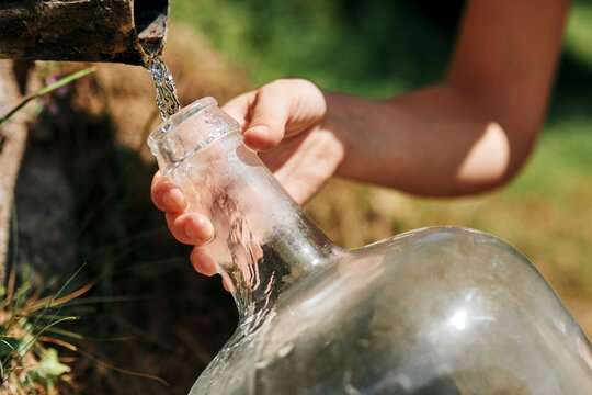 Crop woman filling plastic bottle with fresh water from natural spring in rock in sunny day