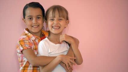Two happy girls hugging each other isolated on pink background