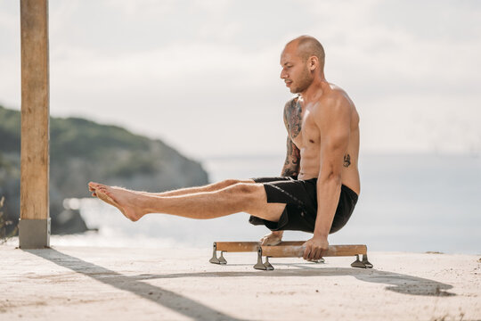 Side view of male athlete with muscular torso performing handstand on parallel bars during workout in summer