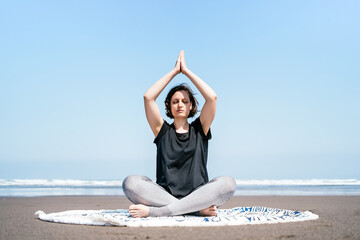 Full body young female in sportswear doing meditation while practicing yoga on sandy seashore