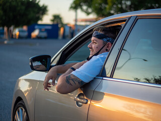 Hombre joven sacando la cabeza por fuera del coche durante su viaje, vistiendo mascarilla