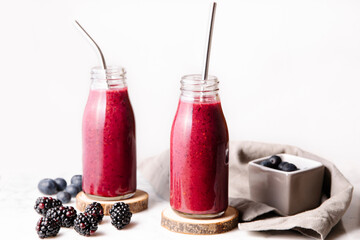 Berry smoothie in glass bottles with reusable metal straws. Front shot with white background.