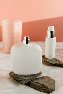 White cosmetic spray bottle and dispenser for cream arranged on stones on marble surface against pink wall