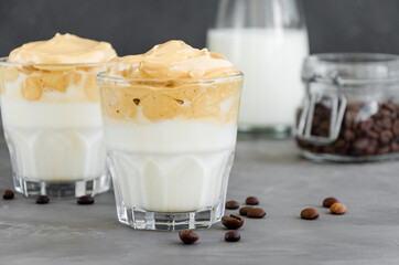 Iced Dalgona Coffee, a trendy fluffy creamy whipped coffee with milk in a glass on a dark background. Horizontal, copy space.