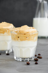 Iced Dalgona Coffee, a trendy fluffy creamy whipped coffee with milk in a glass on a dark background. Vertical, copy space.