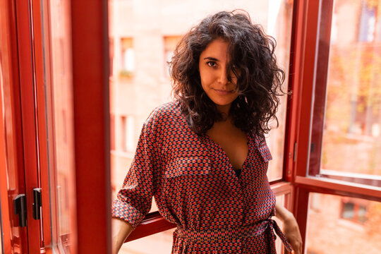 Beautiful ethnic latin woman leaning on windows of her apartment looking at camera