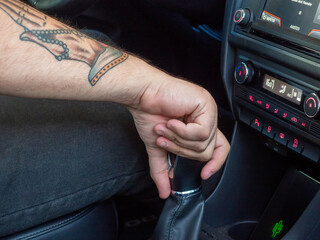 brazo con tatuajes sujetando la palanca de cambio de marchas del coche