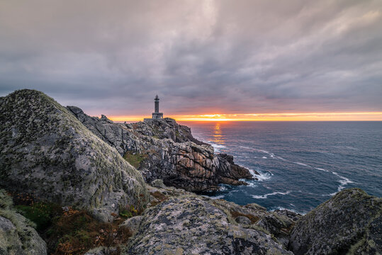 Spectacular scenery of lighthouse located on rough cliff near sea on background of sundown sky