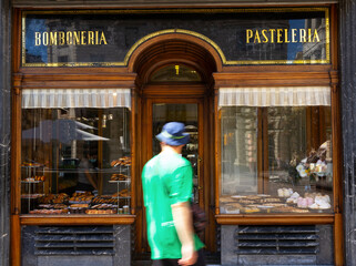 Back view of unrecognizable man walking past showcase with tasty pastry in modern bakehouse located in city