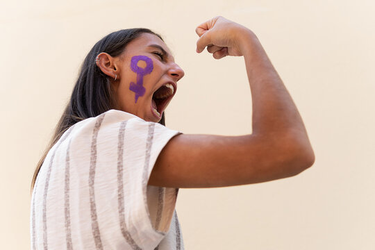 Side view low angle of determined female with gender symbol on face demonstrating muscles while showing girl power concept