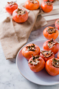 Fresh persimmons on plate placed on white table in bright kitchen
