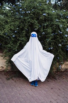 Faceless creepy child in ghost costume standing in park during Halloween on overcast day