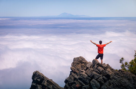 Back view of anonymous male traveler standing with outstretched arms on rocky hill in highlands and enjoying amazing view of clouds