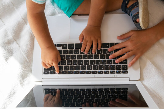 From above young woman and toddler resting on bed and browsing laptop while resting on bed on weekend day together