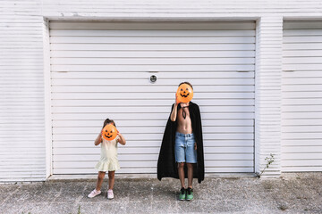 Boy and girl covering their faces with pumpkin shaped balloons on street