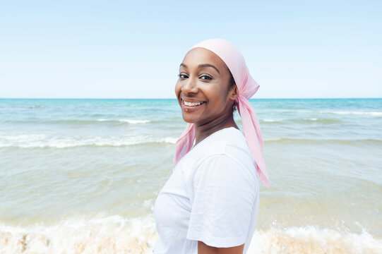Determined ethnic female with headdress and piercing standing on beach on background of sea and looking at camera