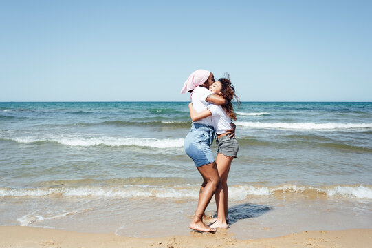 Side view of content African American adult mother and young daughter standing on beach near sea - Powered by Adobe