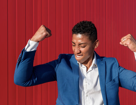 Confident satisfied young African American businessman in formal outfit celebrating success against red wall