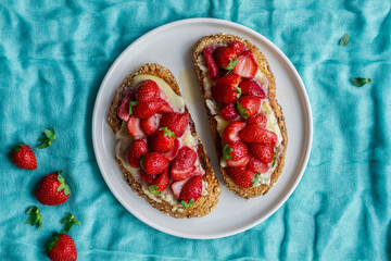 Top view of yummy sweet bread toasts with fresh chopped strawberries and honey served on plate on blue tablecloth