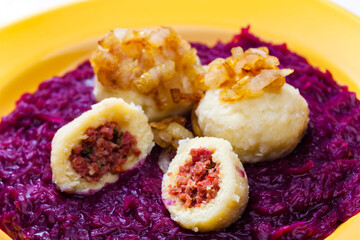 potato dumplings filled with smoked meat with fried onion on red cabbage