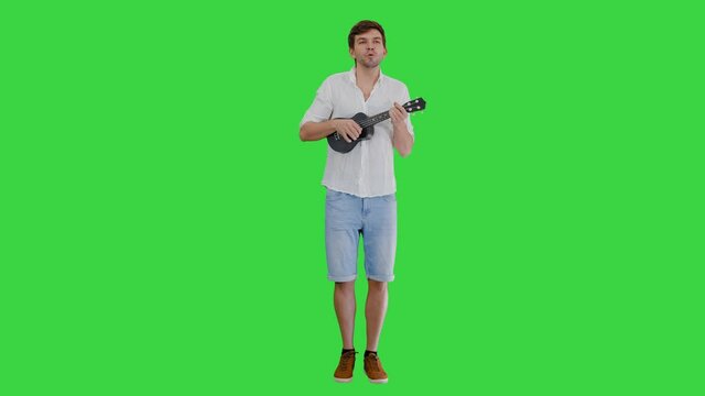 Smiling young man playing ukulele and singing looking into the camera on a Green Screen, Chroma Key.
