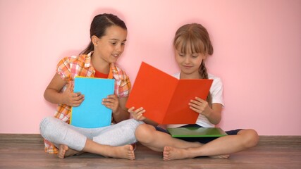 Lovely little girls are reading a book. The concept of education. Isolated on pink background