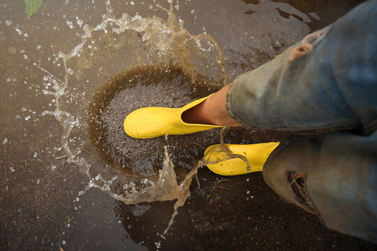 Aerial view of the yellow rain boots hitting a puddle splashing water in a path in the forest