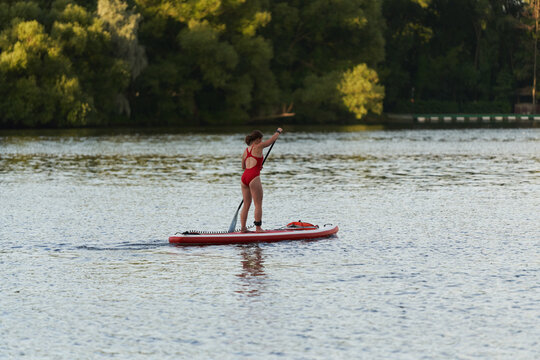 Back view of unrecognizable female surfer standing on surfboard and rowing with paddle while practicing on river in summer