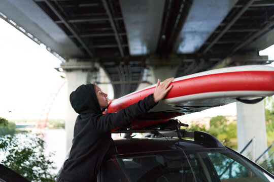 Side view of female surfer putting paddle board on roof of automobile after training