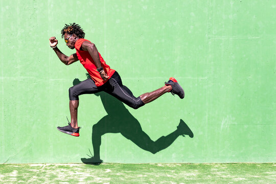 Side view of black sportsman in activewear in moment of jumping during intense workout on sunny day