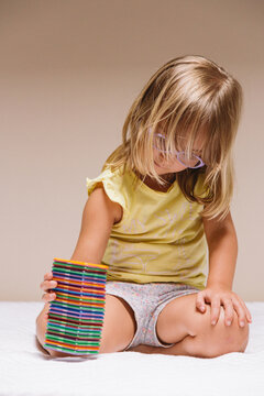 Adorable preschool girl in eyeglasses sitting on floor and playing with colorful educational blocks