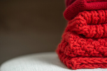 Pile of knitted woolen sweaters red colors. Clothes with different knitting patterns folded in stack. Warm cozy winter and fall knitwear concept. christmas time. close up. mockup. copy space 