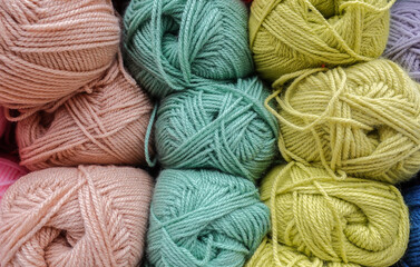 Colorful woolen balls of yarn. Background of colored yarn balls. Needlework. Knitting. Hobbies and leisure. Balls of yarn in light pink, light grey, light green colors.