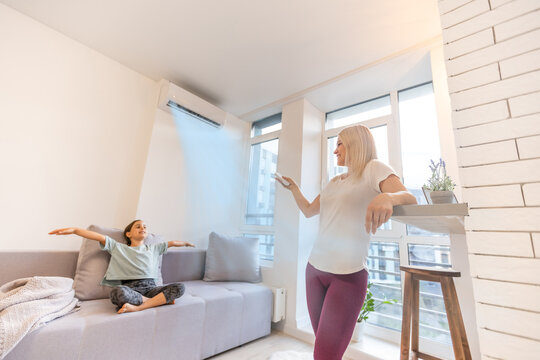 Happy Family Under Air Conditioner, Mom Holding Remote Control Switch On Conditioning In Living Room Adjust Comfort Temperature For Daughter, Climate System At Modern Home