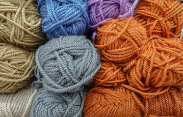 Colorful woolen balls of yarn. Background of colored yarn balls. Needlework. Knitting. Hobbies and leisure. Balls of yarn in orange, blue, khaki, grey and white colors.