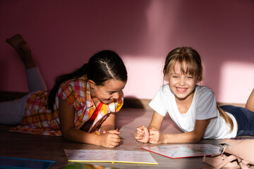 family, leisure and childhood concept - happy sisters lying on floor and doing homework at home