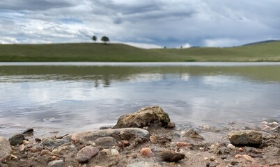 View across lake shore beach with reflective water and green hills in background