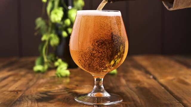 Beer. Cold Craft light Beer in a glass with water drops. Pint of Beer close up on a wooden background. Beer is pouring from the bottle. Border design. High quality 4k footage