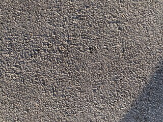 Tiny stones cover textured wall surface in outdoor setting, with bright sunlight and shadow bottom left, creating abstract background pattern